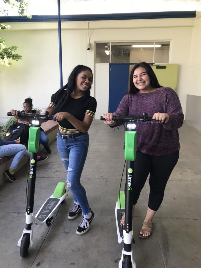 Alexis Smith, left, and Miki Lopez, right, pose with two Lime scooters September 12, 2018 in front of the Main Gym. Recently, students have been riding these scooters to school often. (Nancy Quintana / Lincoln Lion Tales)